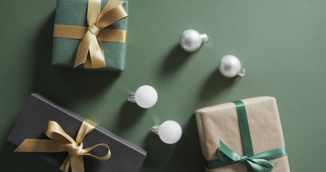 Image showing gift boxes wrapped in elegant ribbons lying on green background, accompanied by festive decorations. Perfect for holiday season promotions, Christmas-themed projects, or celebration invitations. Useful for websites, social media posts, and advertisements related to gift giving and festive occasions.