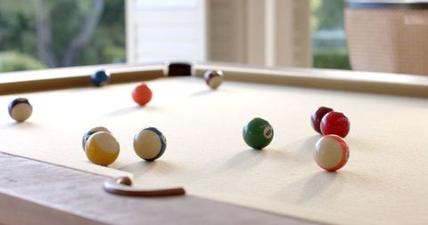 Billiard balls appear to move in tranquil motion on an elegantly lit table in a sunlit room. This image emphasizes recreation and relaxation, creating an inviting atmosphere. Suitable for advertising pool-related games, leisure activities, or interior decor themes showcasing casual sport. Ideal for websites, brochures, or blogs addressing home design, hospitality venues, or lifestyle subjects focused on leisure and sport symbolism.