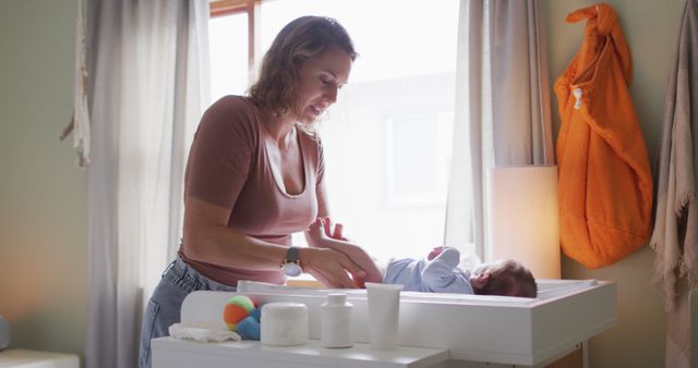 Mother changing diaper of newborn baby in calm, softly-lit nursery. Ideal for content related to parenting, newborn care, mother-child bond, and family routines.