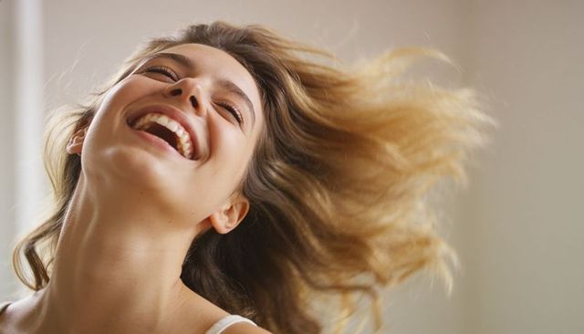 Carefree young woman laughing with windblown hair joyful closeup portrait natural light