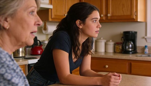 Young woman leaning on kitchen counter listening to senior family member in conversation