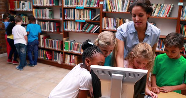 Pupils looking at the computer in library with their teacher in elementary school - Download Free Stock Photos Pikwizard.com