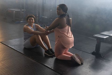 Black female trainer assisting client performing sit-ups in gym for inclusive fitness