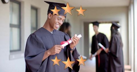 Graduating student smiling while inspecting diploma ribboned with red bow, celebratory stars