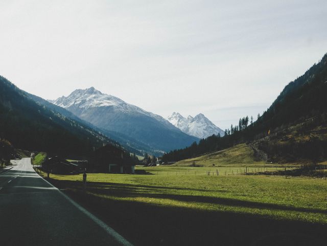 Peaceful road winding through a picturesque valley with snow-capped mountains in the distance. Ideal for travel and adventure promotions, nature documentaries, landscape photography, and outdoor lifestyle brands.