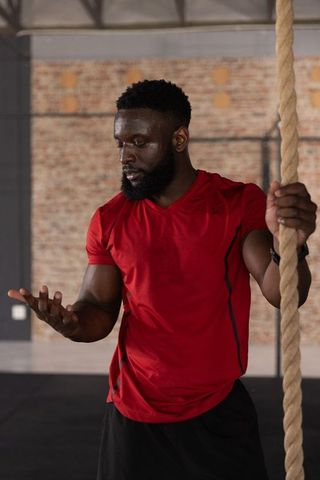 African american man holding climbing rope checking palm after intense gym workout