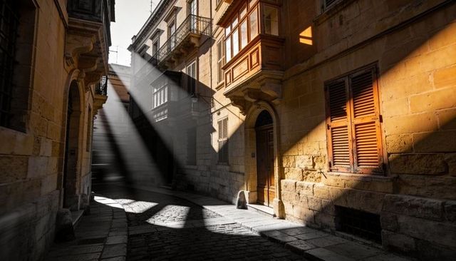 Sunlight beams streaming through narrow mediterranean alley highlighting limestone facades