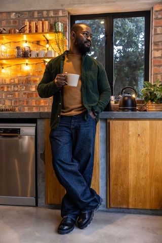 African american man standing in cozy brick kitchen holding mug, gazing out window