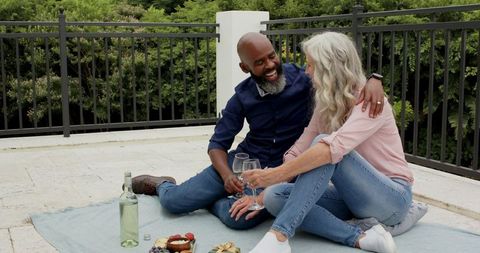 Smiling couple enjoying wine and snacks on sunny terrace picnic