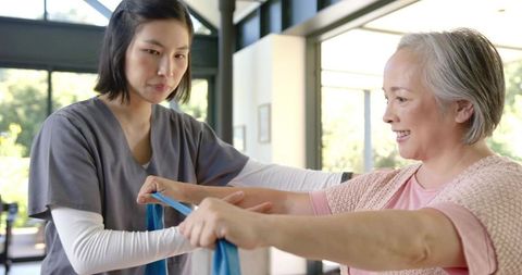 Caregiver assisting senior performing resistance band rehabilitation exercise in clinic
