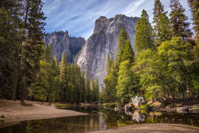 Mountains rising above pine trees reflecting on a calm river in Yosemite National Park, showcasing natural beauty. Ideal for promoting nature tourism, outdoor adventures, and travel destinations. Suitable for use in travel brochures, blogs, or environmental conservation campaigns.