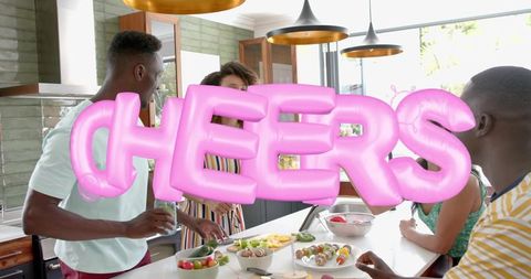 Friends gathering in modern kitchen preparing skewers with pink cheers balloon