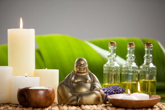 Laughing buddha figurine, lit candle, massage oil bottles and sea salt on mat