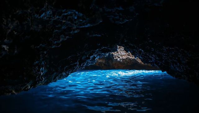 Framing arched sea cave revealing luminous azure water and rock beyond, glowing reflections