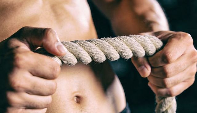 Muscular male gripping heavy battle rope showing frayed fibers and defined torso closeup