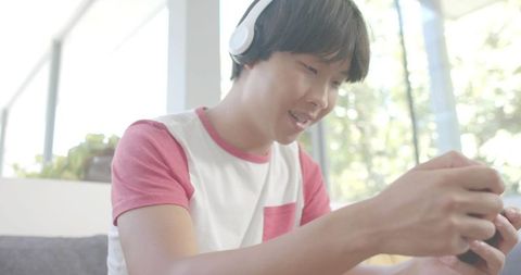 Young man playing mobile game on couch with headphones, casual indoor gaming lifestyle
