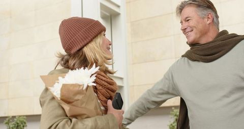 Senior couple greeting at doorstep holding bouquet and phone smiling reunion