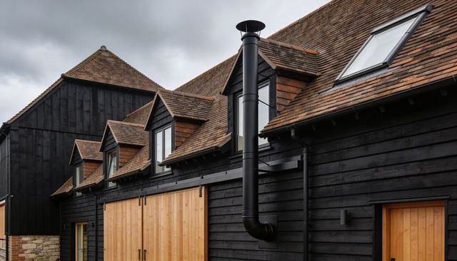 Showcasing dark-clad barn with sliding timber doors, dormer windows and black flue