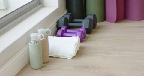 Sunlit home workout corner showcasing dumbbells, water bottles and folded towel