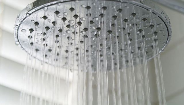 Modern chrome rainfall showerhead streaming water droplets close-up bathroom fixture