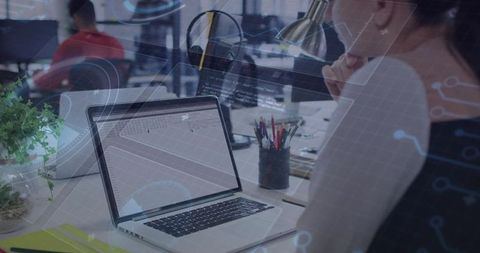 Working woman leaning over laptop analyzing spreadsheet in coworking office with tech overlay