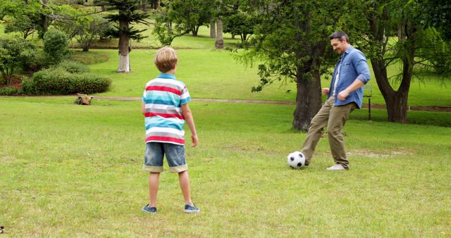 Father and son kicking a football back and forth in the park on a sunny day