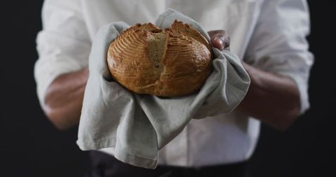 Artisan baker holding freshly baked rustic bread loaf