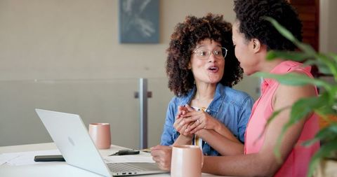 Two women collaborating on laptop with coffee at home office