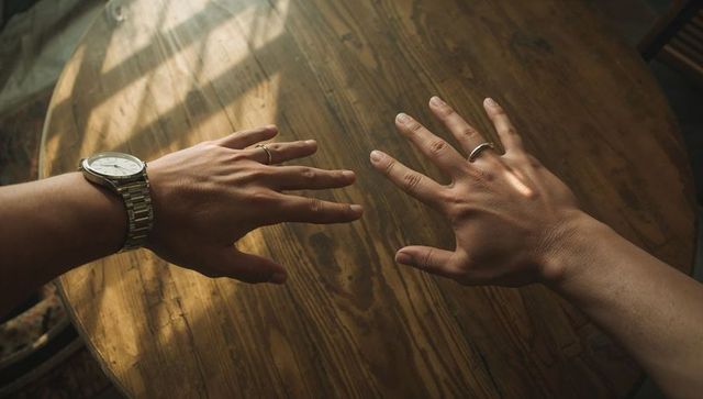 Resting Hands on Sunlit Wooden Table with Watch and Wedding Rings, Intimate Closeup