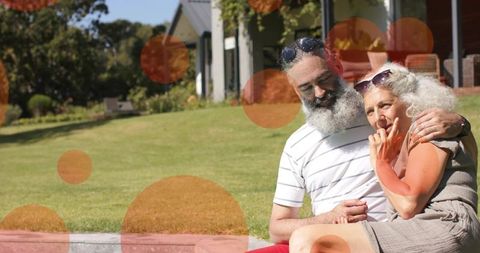 Senior couple embracing on lawn near home porch enjoying sunlit afternoon