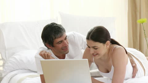 Happy Couple Relaxing in Bed Using Laptop Together