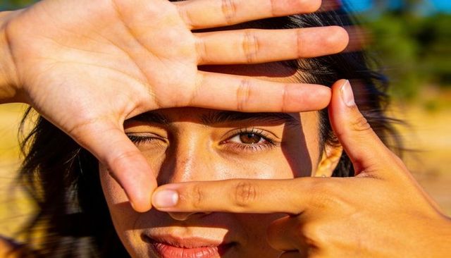Framing woman with hands revealing single eye during golden hour beach closeup portrait