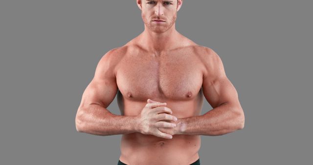 A fit, shirtless man with a muscular body poses confidently with his hands clasped. Ideal for use in fitness promotions, advertisements, health magazines, gym posters, or motivational workout materials.
