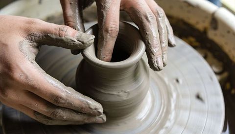 Hands shaping clay vase on spinning pottery wheel, artisan thinning rim closeup