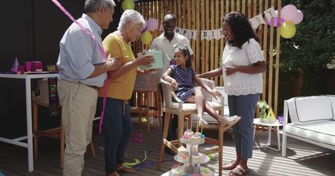 Multi-generational family celebrating backyard birthday on wooden deck with cupcakes