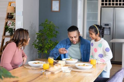 Family sharing warm breakfast around wooden dining table with orange juice, bread, smiles