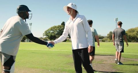 Cricket players shaking hands after match on sunny community field showing sportsmanship