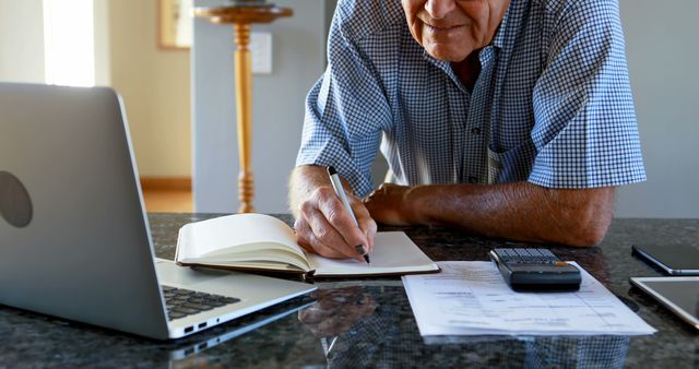 A senior man is diligently managing finances or tasks at his kitchen workspace. - Download Free Stock Photos Pikwizard.com