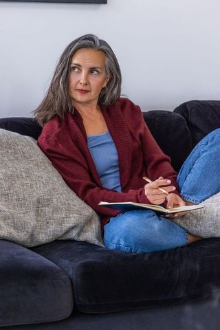 Middle-aged woman journaling on couch, relaxed self-reflection in cozy living room