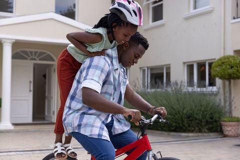 African american father teaching daughter to ride bicycle on suburban driveway
