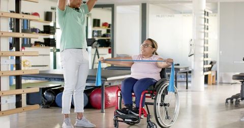 Therapist Assisting Woman in Wheelchair with Resistance Band
