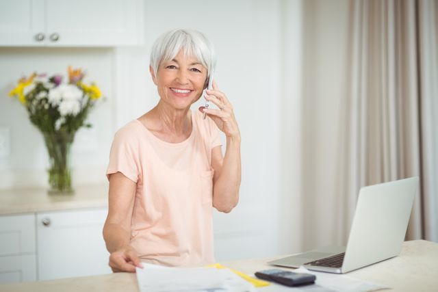 Portrait of senior woman talking on mobile phone in kitchen at home