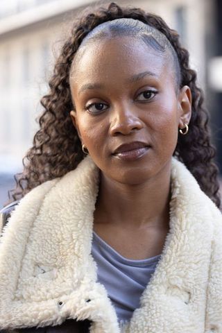 Stylish african woman wearing cream shearling jacket and gold hoops on urban street