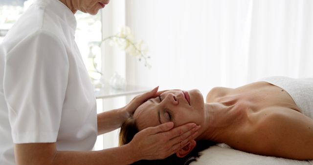 A middle-aged Caucasian woman receives a relaxing facial massage from a professional therapist, with copy space. Capturing a moment of tranquility, the image reflects the therapeutic and wellness industry.