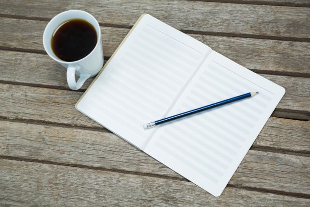 Black coffee with notebook and a pencil kept on wooden surface