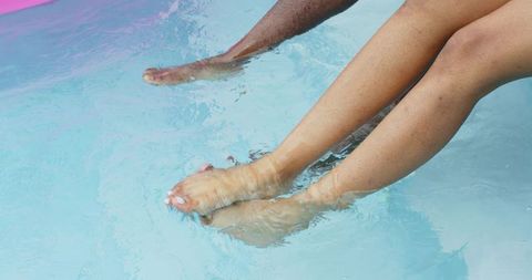 Diverse couple relaxing with legs dangling in clear blue pool near pink edge summer leisure