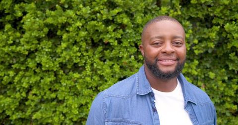 African american man smiling outdoors in denim shirt with green hedge background casual portrait