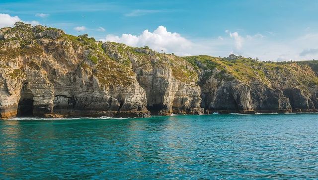 Dramatic limestone cliffs revealing sea caves and arches above turquoise coastal waters