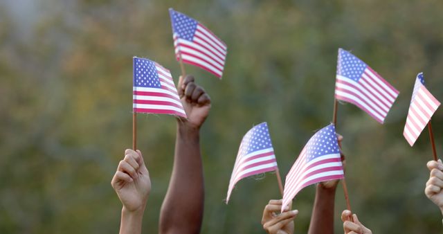 Hands of diverse individuals holding small American flags at an outdoor event. This portrays a sense of unity, national pride, and patriotism. Ideal for use in content related to Independence Day celebrations, patriotism, community events, or in campaigns promoting unity and diversity in the U.S. Great for social media, blogs, or advertisements showcasing American pride.