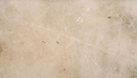 Worn beige marble countertop showing scratches, stains and patina texture